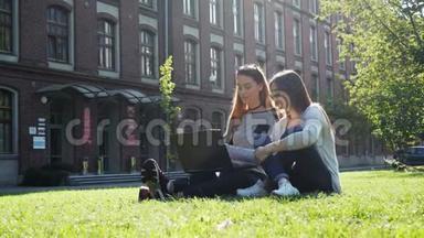 两个漂亮而现代的女学生或自由职业者在笔记本电脑上工作，<strong>坐在</strong>校园绿色草坪上的<strong>公园里</strong>